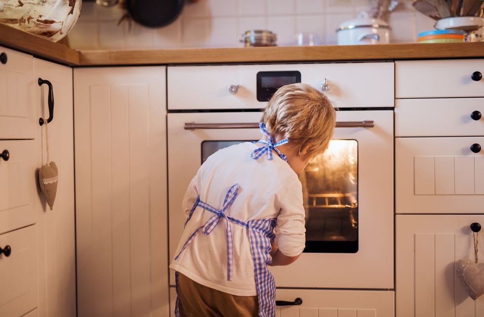 A rear view of small boy looking in the oven indoors, baking.