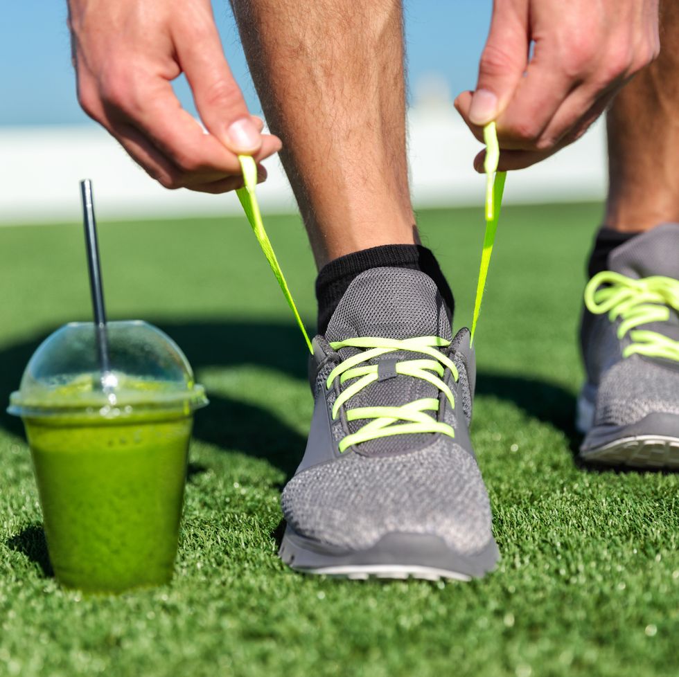 green smoothie fitness man lacing running shoes, athlete runner with green vegetable detox juice getting ready for morning run tying running shoe laces on grass fitness and healthy lifestyle concept