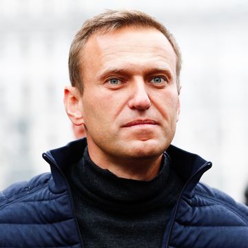 alexei navalny stares forward with a neutral express, he wears a blue puffy jacket and black turtleneck sweater