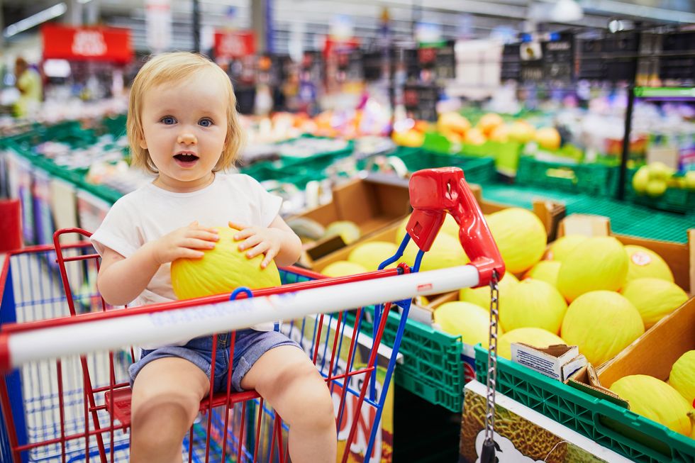 adorable toddler girl sitting in the shopping cart in a food store or a supermarket little kid going shopping