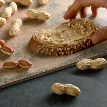 a male hand holding peanut butter bread with shelled peanuts