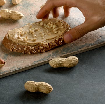 a male hand holding peanut butter bread with shelled peanuts