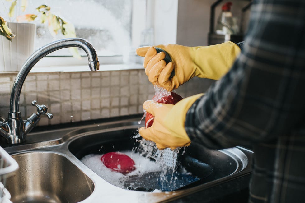 man standing at the sink, wearing yellow marigold gloves, washing the dishes.