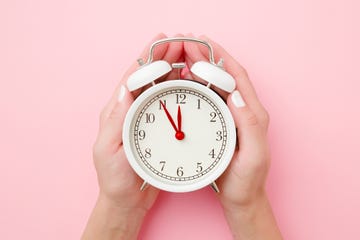 woman hands holding white alarm clock on light pastel pink background time concept closeup top view