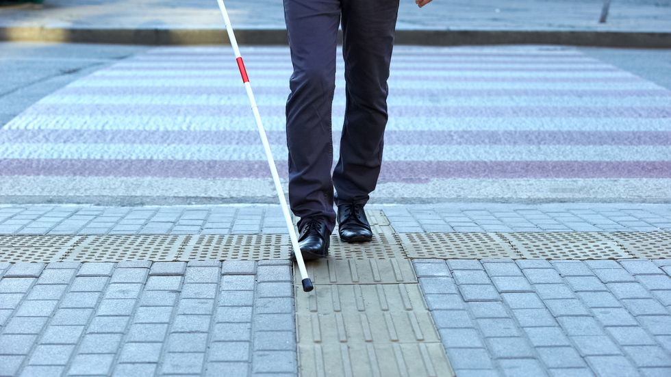 visually impaired man using tactile tiles to navigate city, finishing crossroad