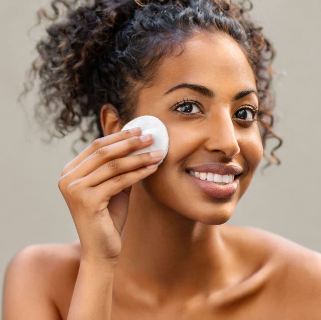 young pretty african american woman taking off her makeup with cotton wipe sponge smiling girl cleaning face with cotton pad isolated over background black young woman cleansing face, daily healthy beauty routine