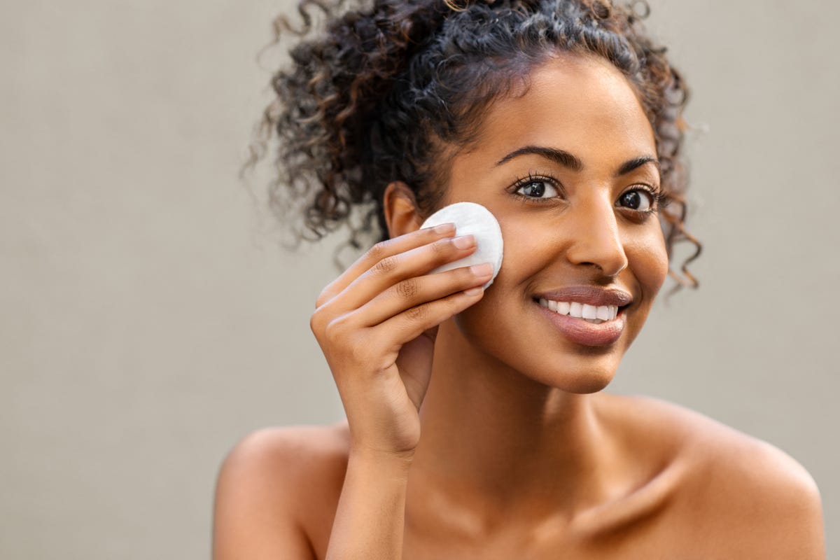 young pretty african american woman taking off her makeup with cotton wipe sponge smiling girl cleaning face with cotton pad isolated over background black young woman cleansing face, daily healthy beauty routine