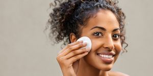 young pretty african american woman taking off her makeup with cotton wipe sponge smiling girl cleaning face with cotton pad isolated over background black young woman cleansing face, daily healthy beauty routine