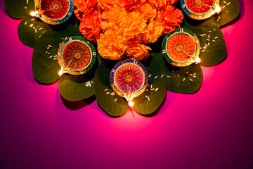 happy dussehra clay diya lamps lit during dussehra with yellow flowers, green leaf and rice on pink pastel background dussehra indian festival concept