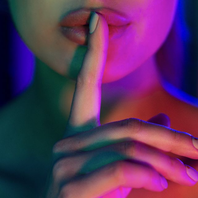 silent gesture woman holding finger on lips in colourful neon lights, closeup