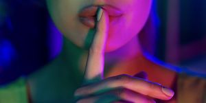 silent gesture woman holding finger on lips in colourful neon lights, closeup