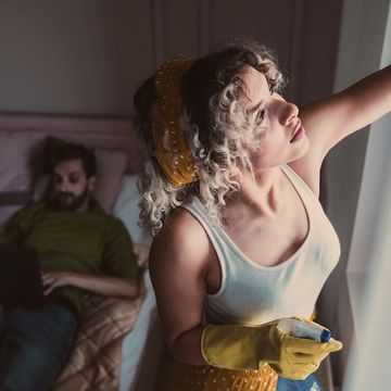 woman cleaning room while husband lying on the bed