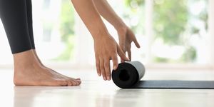 Young woman rolling black yoga mat side view close up