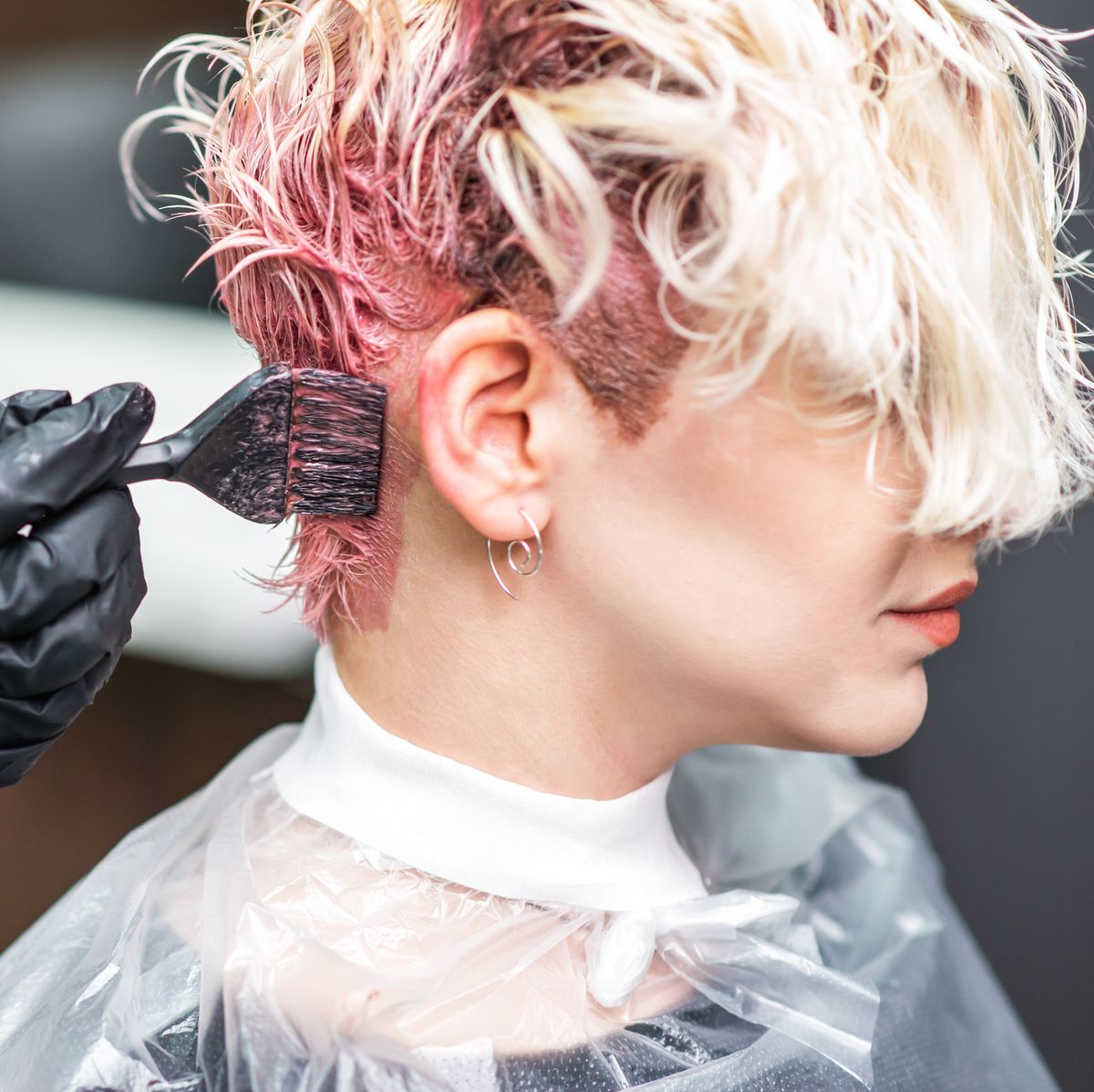 Hairdresser hand in black gloves paints the woman's hair in a pink color.