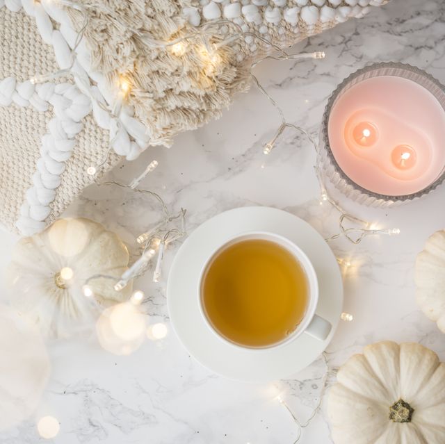 festive autumn flat lay still life with twinkling party lights and white ornamental gourds around a cup of hot tea and candles