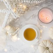 festive autumn flat lay still life with twinkling party lights and white ornamental gourds around a cup of hot tea and candles