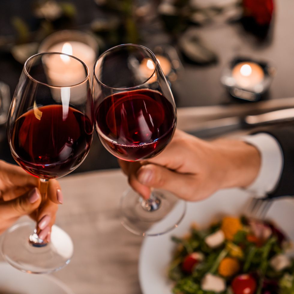 close up of young couple toasting with glasses of red wine at restaurant