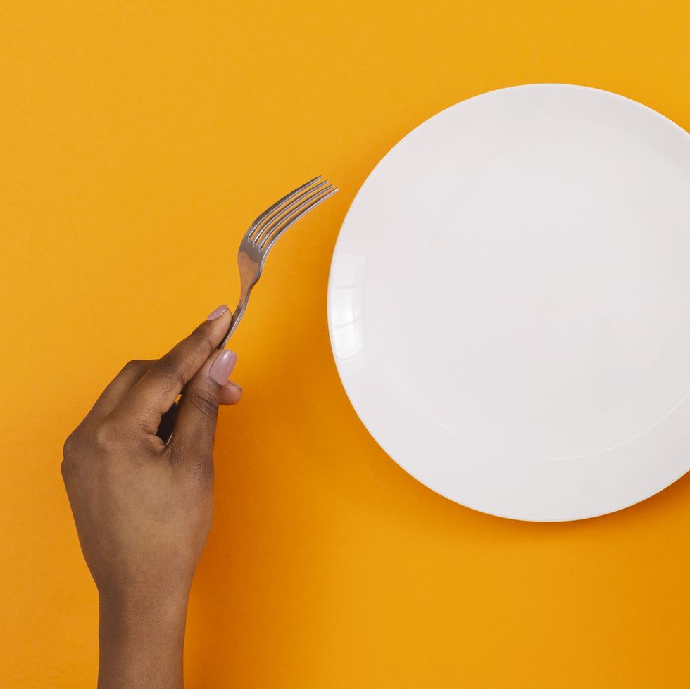 lunch time top view of empty plate with fork and knife in black womans hands on orange background, panorama