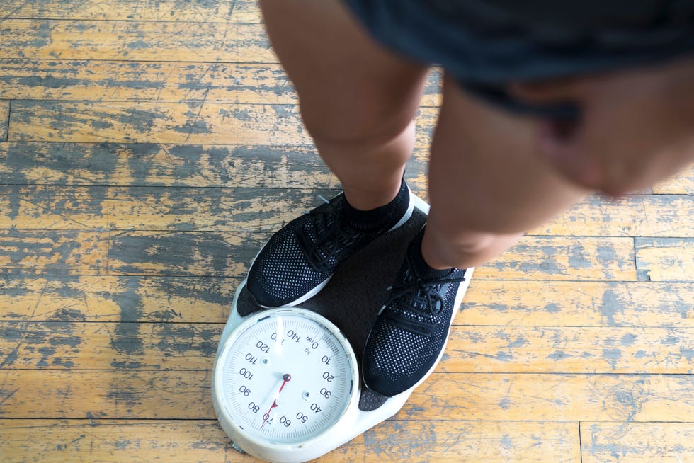 low section of man checking weight on scale in gym men's health