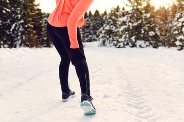 person stretching in winter attire on a snowy path