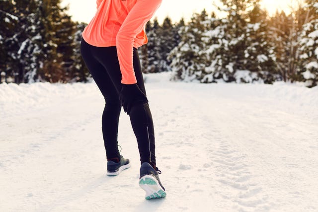 person stretching in winter attire on a snowy path