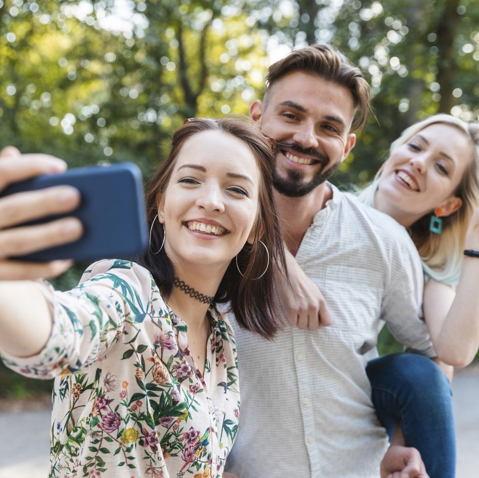 group of three friends taking selfie with smartphone