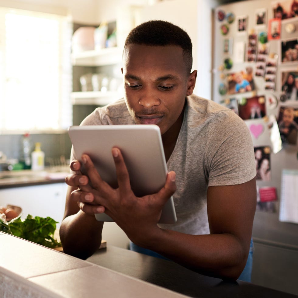 cropped shot of a handsome young man using a digital tablet while making breakfast in his kitchen at home