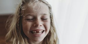 Portrait of young freckled smiling girl missing tooth with eyes closed