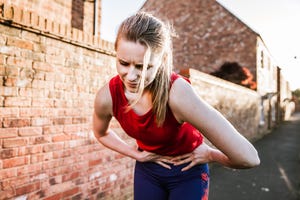 sporty woman outdoors, holding her stomach in pain