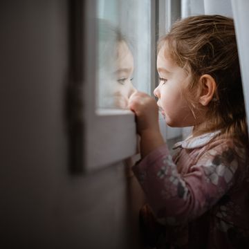 Side view of young girl looking outside window at rain