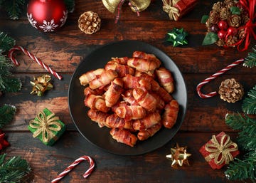 Christmas Pigs in blankets, sausages wrapped in bacon with decoration, gifts, green tree branch on wooden rustic table