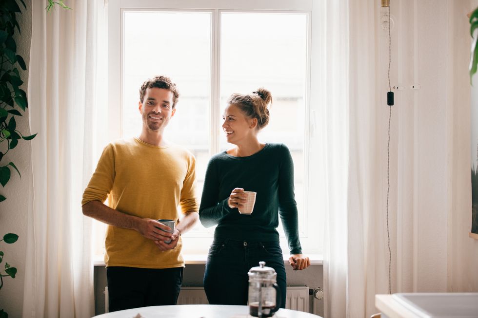 Happy couple with coffee mug against window at home