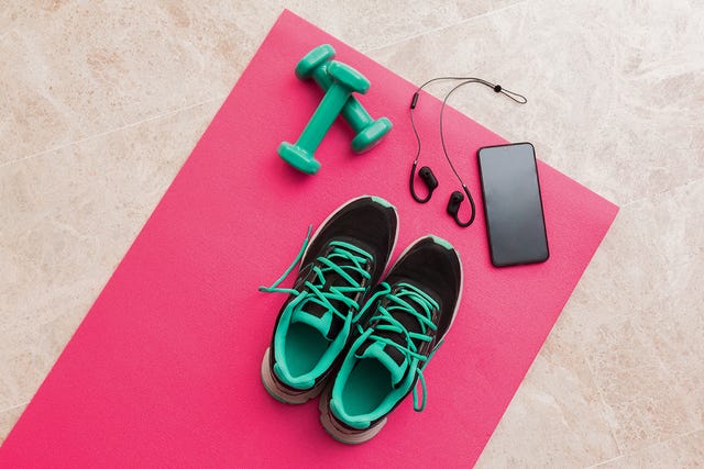 fitness gear including shoes dumbbells headphones and a smartphone on a yoga mat