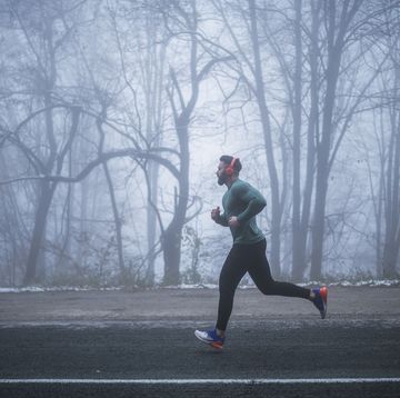 full length man wearing sports clothing and red headphones running antic on the road in foggy weather condition