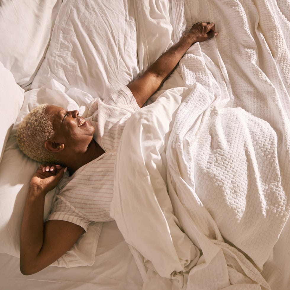 a mature woman wakes up and stretches in early morning light