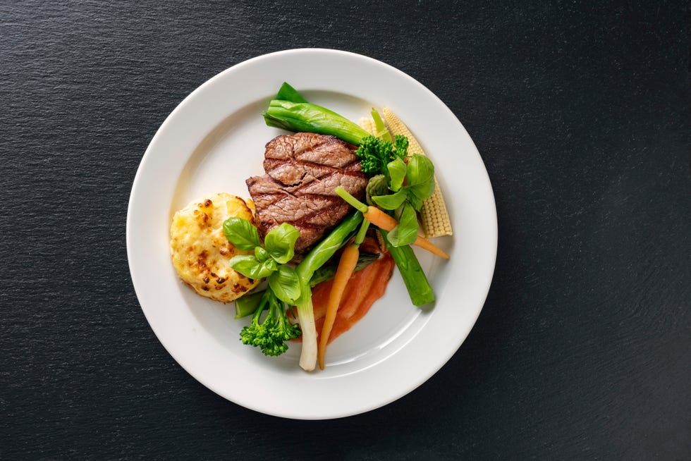 overhead view of a main course dish of veal tenderloin with seasonal vegetables which include carrots and leeks with a potato gratin and a tomato sauce colour, horizontal with some copy space shot on location in a restaurant on the island of moen in denmark