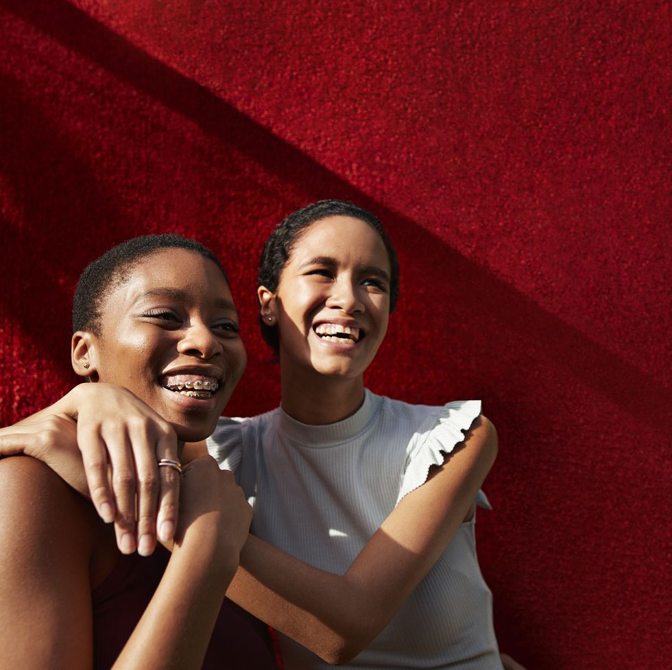 smiling young woman standing with female friend against red wall