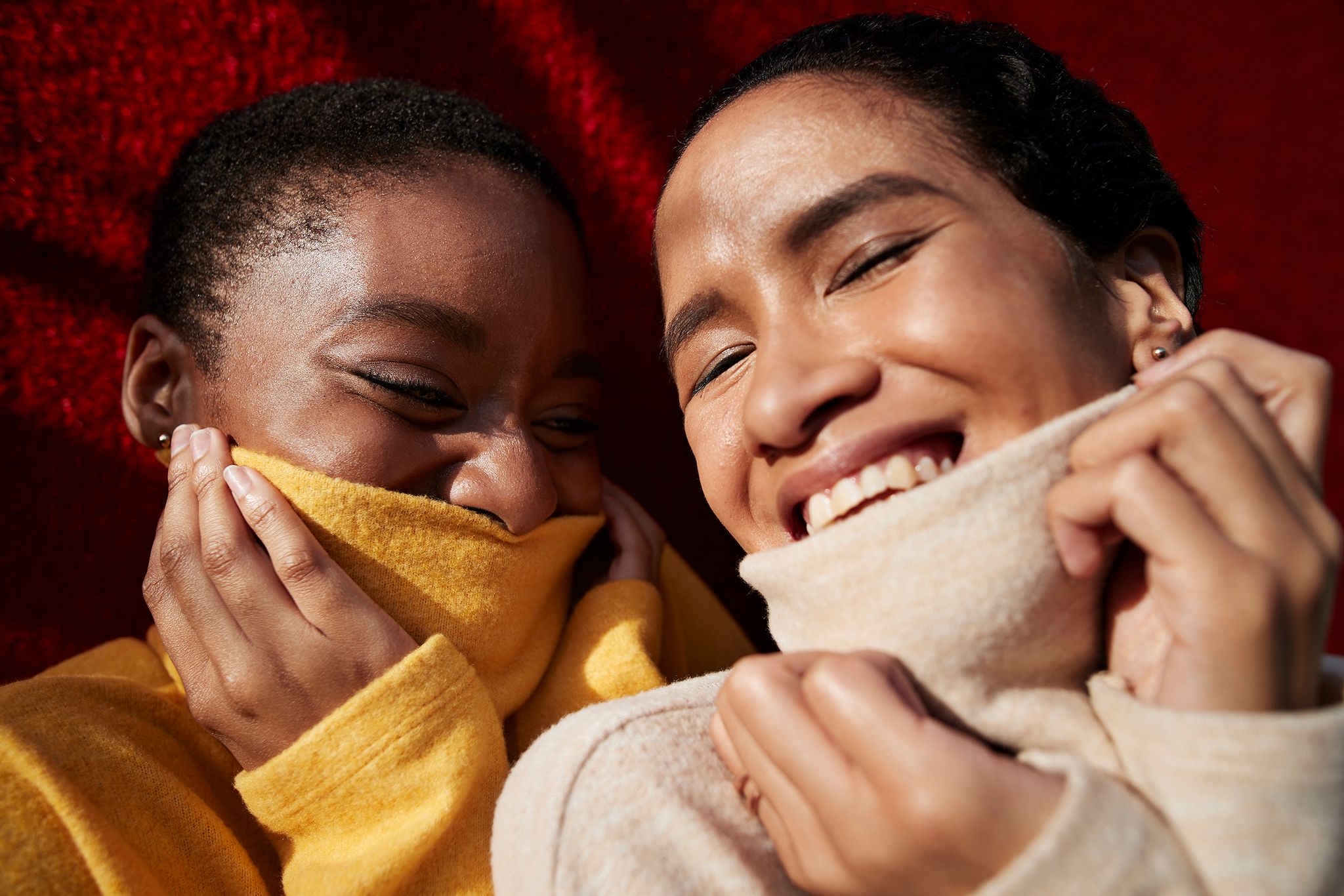 smiling young female friends wearing turtleneck sweaters against red wall