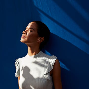 thoughtful young woman standing against blue wall