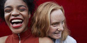 close up of young women laughing while standing against red wall