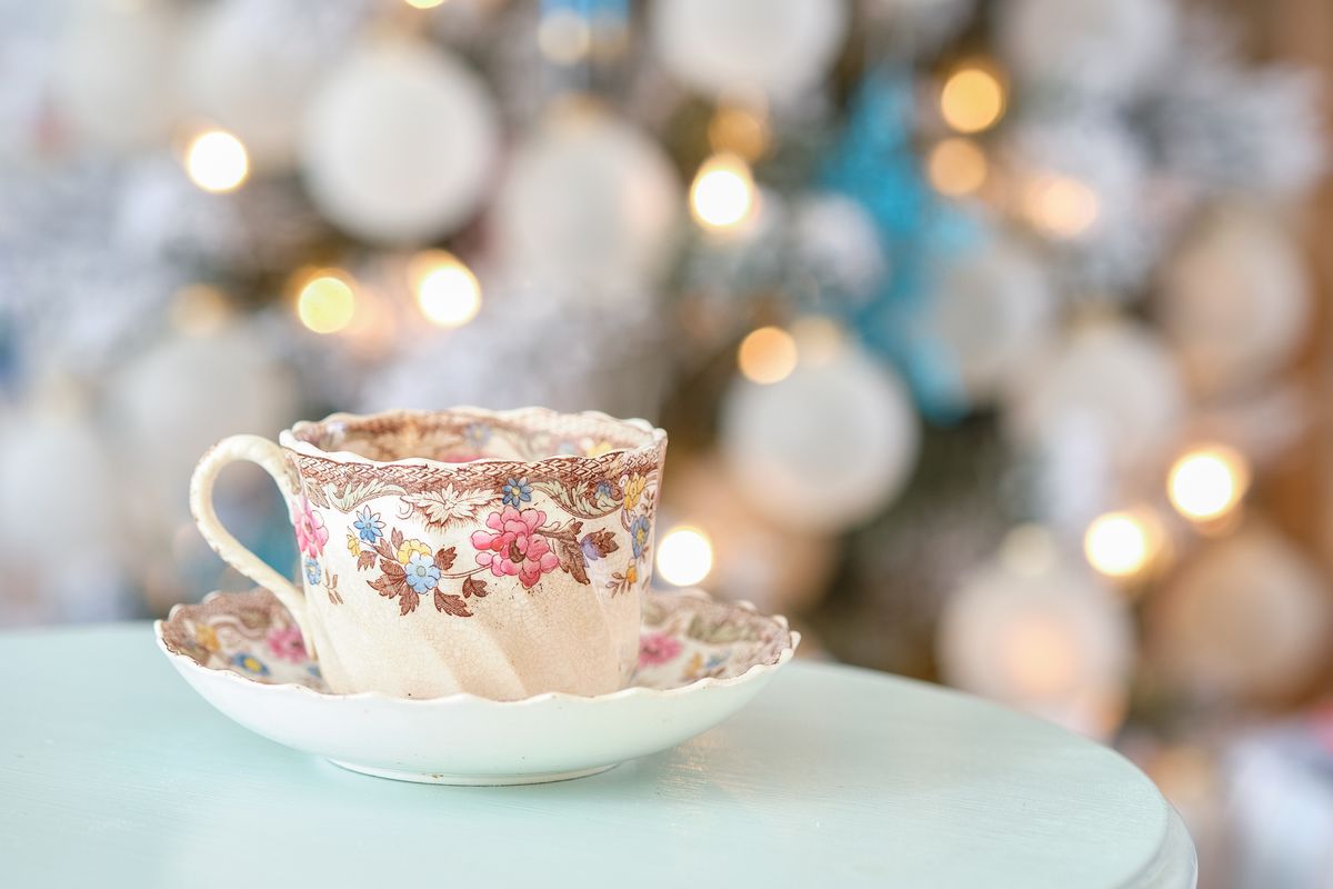 steam streams out of a colorful english tea cup on a teal table in front of a decorated christmas holiday tree