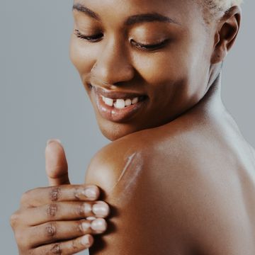 applying lotion to her shoulder against a gray studio background