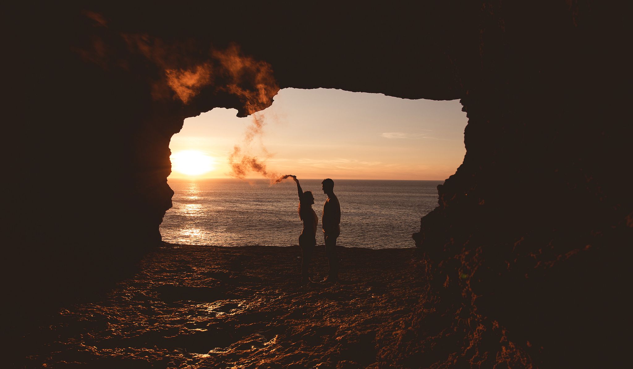happy couple in love with a smoke flare, in a natural cave near the sea