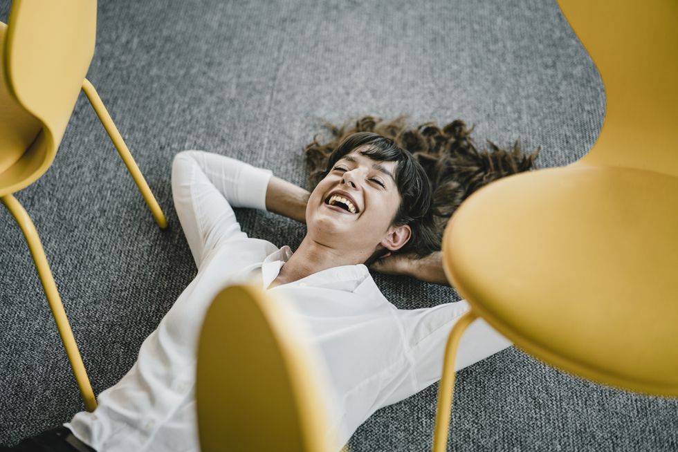 laughing businesswoman laying in an office on the floor between chairs