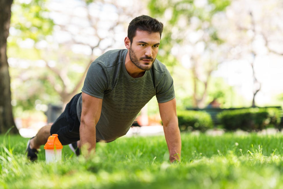 a handsome young man doing push ups in the park he has a protein drink right next to him