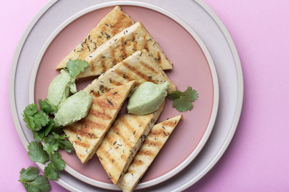 grilled herbed tofu with avocado cream,  vegan meal served  with fresh cilantro herbs, plant based food on pink background
