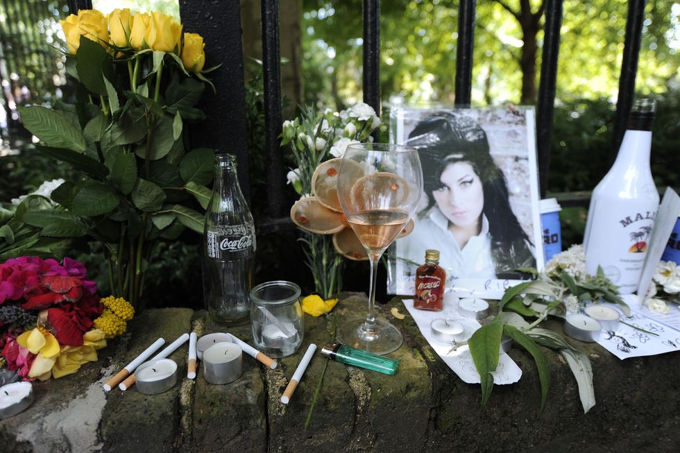 cigarettes, candles, alcohol, flowers, messages and a photo of amy winehouse rest on a stone wall outside
