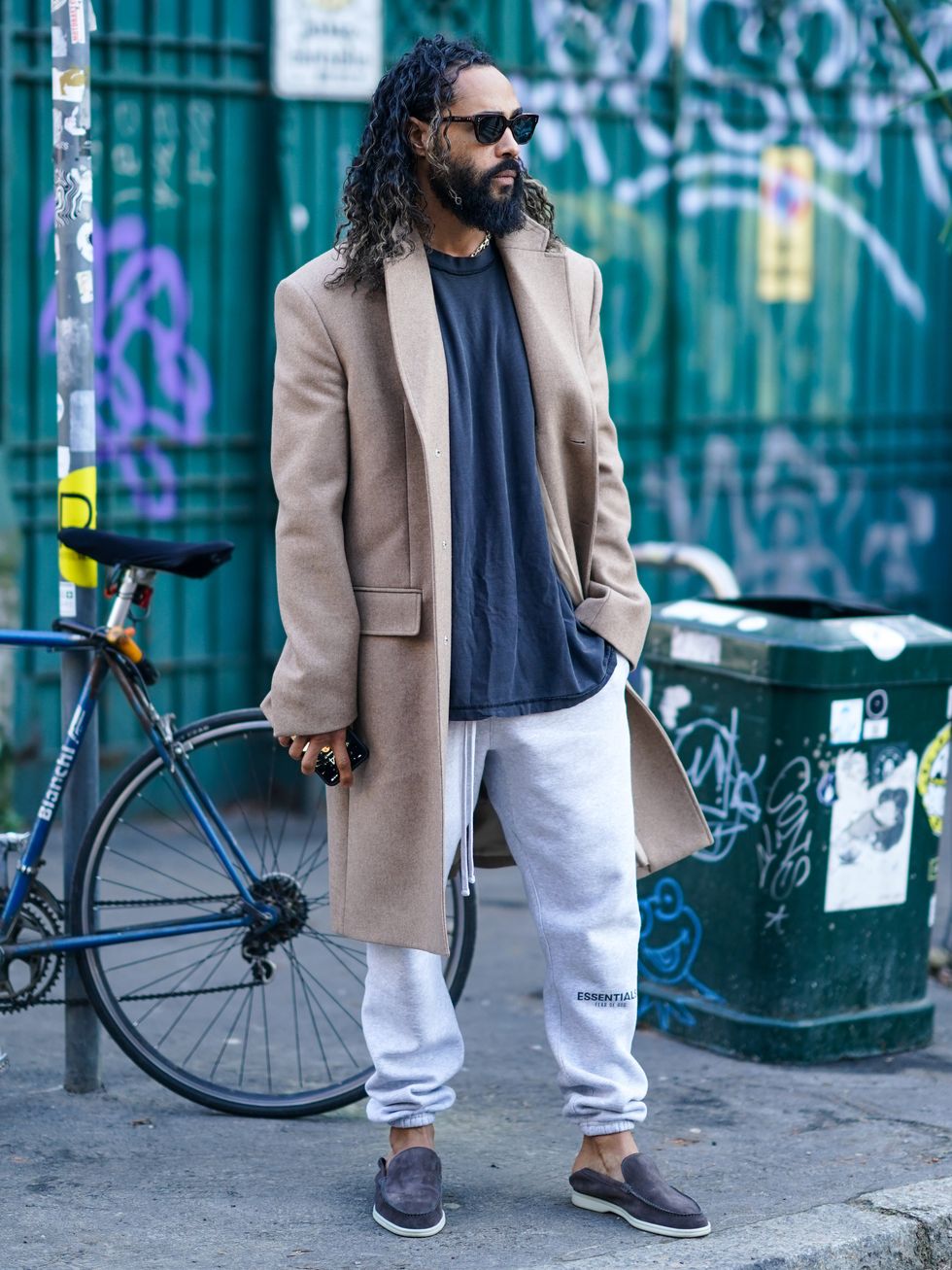milan, italy   january 11  jerry lorenzo wears sunglasses, a beige long coat, a gray t shirt, white "essential fear of god" sportswear pants, suede shoes, outside marni, during milan fashion week fallwinter 20202021, on january 11, 2020 in milan, italy photo by edward berthelotgetty images