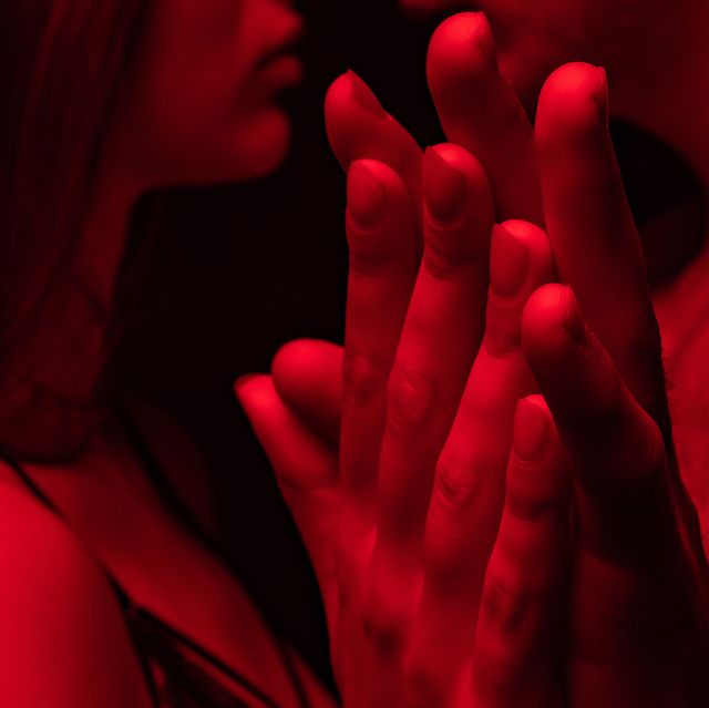 side view of passionate undressed sexy young couple kissing and holding hands in red light isolated on black