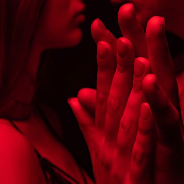 side view of passionate undressed sexy young couple kissing and holding hands in red light isolated on black